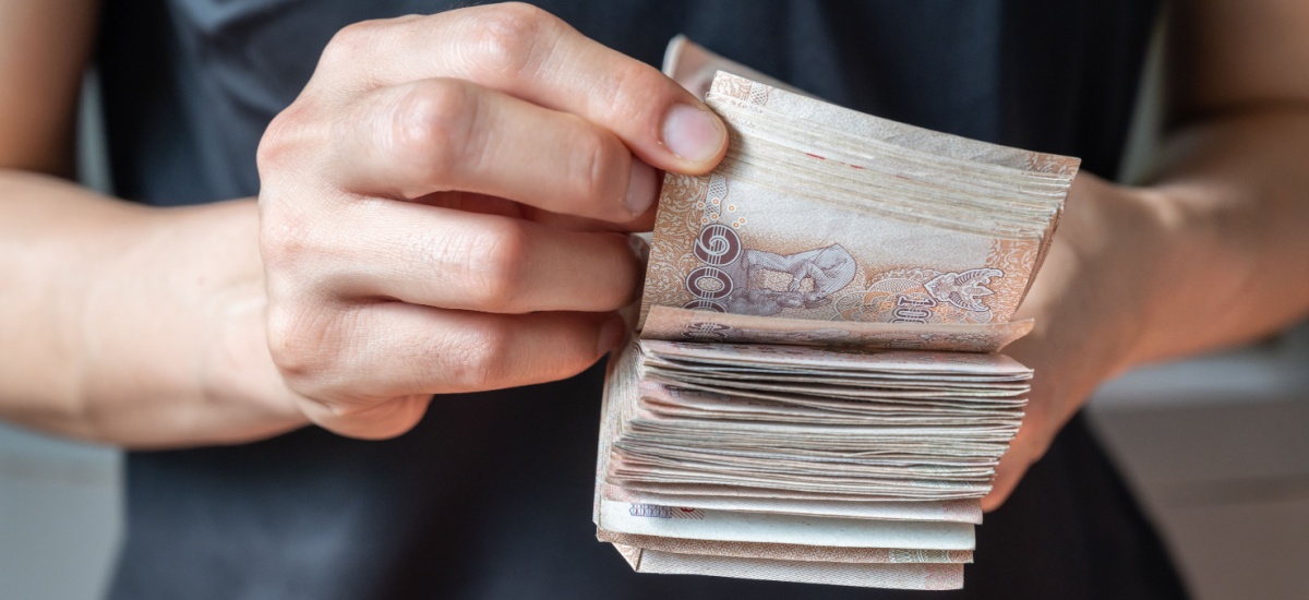 close up of a hand counting a large wad of Thai baht